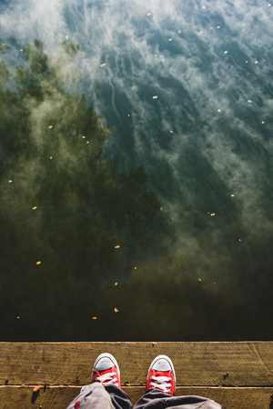 A man standing on the wooden pier.  A reflection of cloud and tree on the water and a man standing on the wooden pier background with copy space.の写真素材