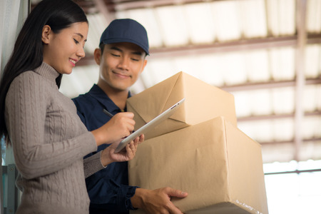 Woman customer signing receipt and receiving the parcel from delivery man. Business and logistic concept.の写真素材