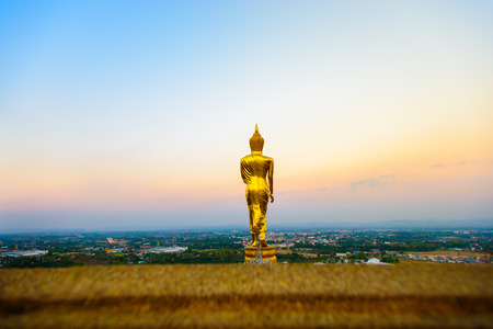 The sacred standing statue of Buddha at Wat Phra That Khao Noi in Nan, north of Thailand with vivid sunrise sky background.の写真素材
