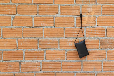 Leather bag hanging on orange brick wall.の写真素材