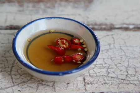 Fish sauce and chili in white cup on old wooden table.