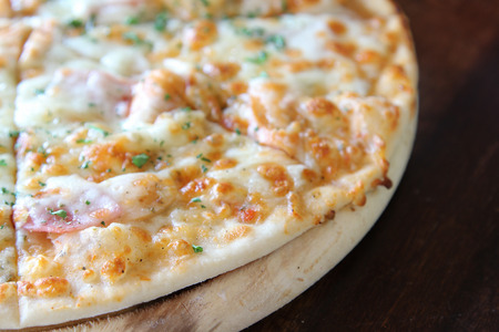 Sliced pizza with ham, sausage and vegetables on wooden tray.の写真素材