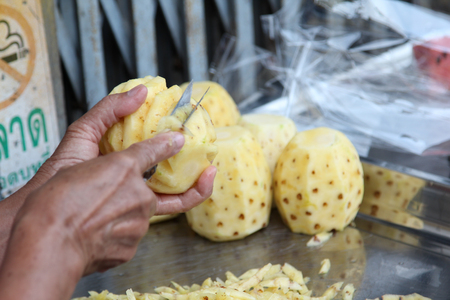 Male's hands peeling pineapple fruit then put it on the stainless steel tray.の写真素材
