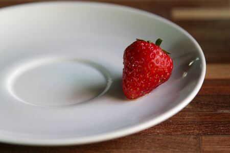 A juicy fresh strawberry on a white ceramic plate.の写真素材