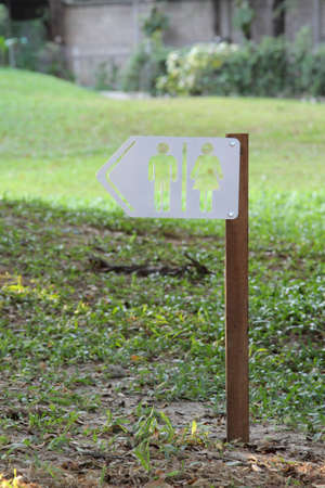 White toilet sign on wooden pole on green grass.
