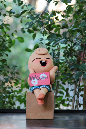 A clay doll children boy sitting with a welcome sign.