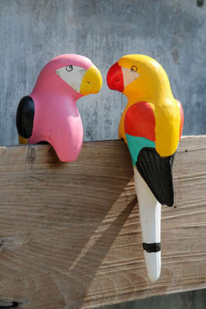Small colorful parrots sculpture perched on a wooden board.の写真素材