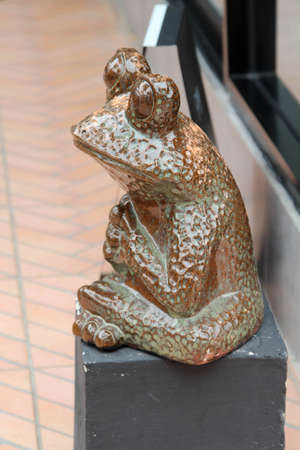 A brown frog statue sitting on a gray concrete podium.の写真素材