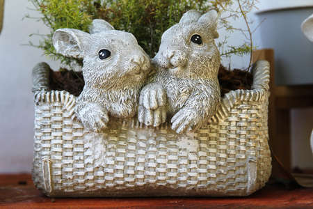 Small ceramic plant pots and rabbit statue on a wooden shelf on white concrete wall.の写真素材