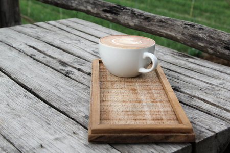 Hot cappuccino with heart shaped latte art on wooden plate on old wooden tableの写真素材