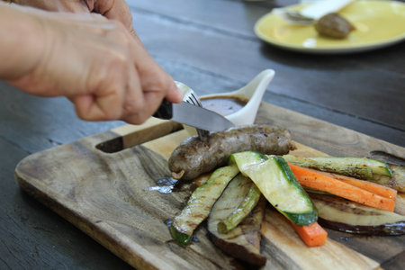 Sausage and fried vegetable served with sauce on wooden plateの写真素材