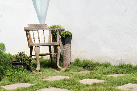 A wooden chair on green grass in front of white concrete wallの写真素材