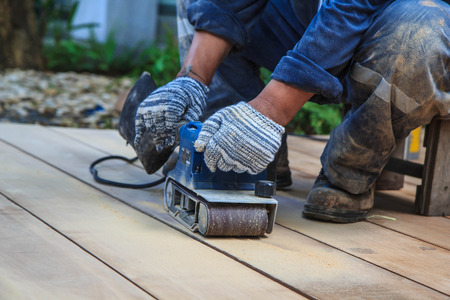 Carpenter working with electric planer on wooden plank outdoor.の写真素材