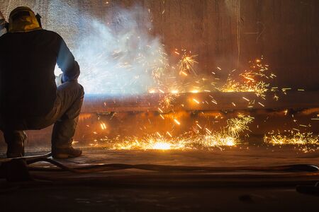 Male worker wearing protective clothing and repair welding tank shell plate storage fire and smoke...