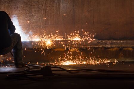 Male worker wearing protective clothing and repair welding tank shell plate storage fire and smoke...
