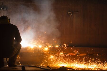 Male worker wearing protective clothing and repair welding tank shell plate storage fire and smoke...