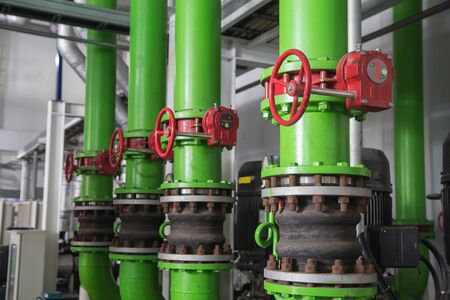 Steel pipelines green and valves red against industrial zoneの写真素材