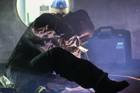 Male  worker wearing protective clothing and repair  welding tank bottom plate storage tank inside...