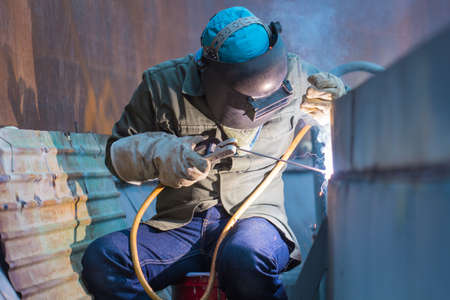 Male  worker wearing protective clothing and repair welding patition plate industrial construction oil and gas or  storage tank inside confined spaces.の写真素材