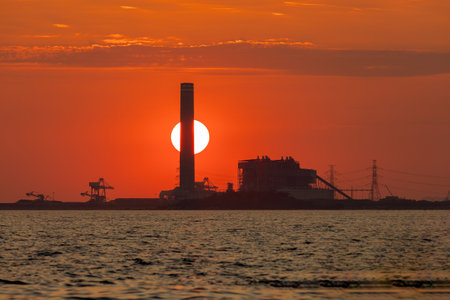 Sunset behind an industrial factory and in front is the sea, orange color, silhouetteの写真素材