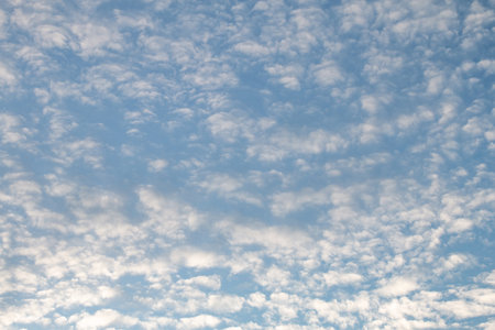 The blue sky was dotted with small fluffy white cloudsの写真素材