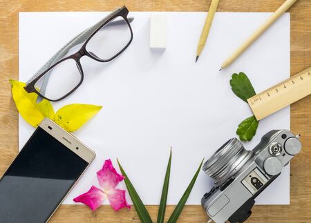 Top view White paper is placed on a wooden floor. There are cameras and phones and pencil , glasses, The eraser ruler is placed on a wooden floor table.の写真素材