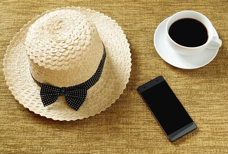 A hat with a cup of coffee, and a phone placed on the work area.