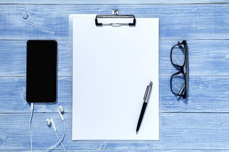 Top view desk, blue floor with clipboard, phone, earphone, eyeglasses and pen placed on the desk.の写真素材
