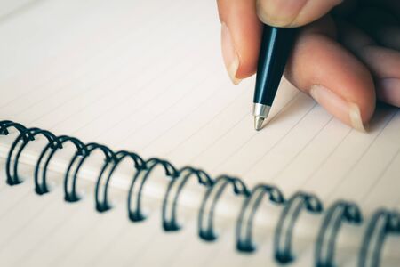 Woman hand with pen writing on white notebook. Focus on the tip of the pen being written. with copy...