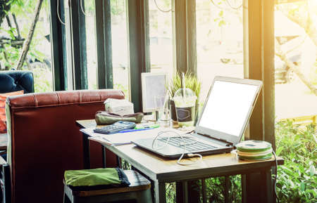 Laptop computer with opened on wood table in room of workspace. Glass window work deskの写真素材