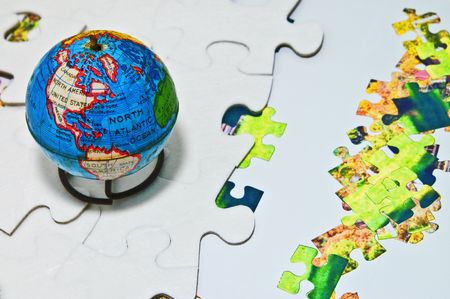 An old world globe on top of white and colored puzzle pieces.  Concept or metahor of keeping up with the changes in the world and trying to add more green pieces to the puzzle to help the planet.の写真素材