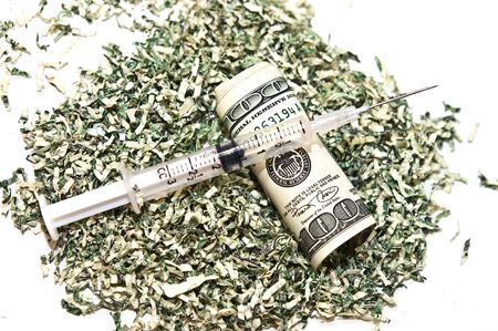 Shredded money, a 100 dollar bill, and a syringe.  Concept or metaphor for cost of drugs, health, wasting money on drugs, medical plans, etc.の写真素材