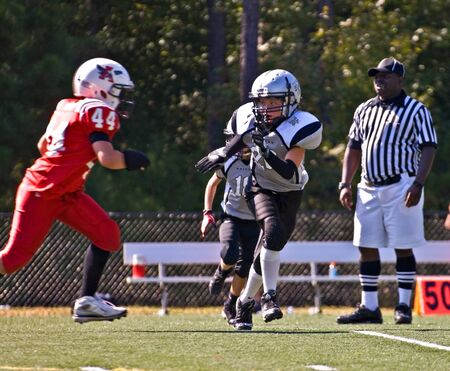 Forsyth County, Cumming, GA - October 30,2010- A blocker running to make a tackle on the opposition, with a referee looking on.  A regular season game between the Raiders and the John's Creek Gladiators.のeditorial素材