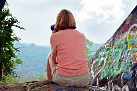 Woman sitting on rocks on a mountain taking an aerial photograph.の写真素材
