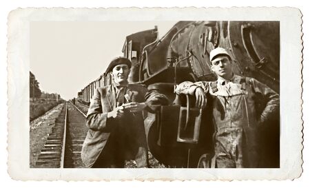 A vintage snapshot of two men standing at an old engine.のeditorial素材