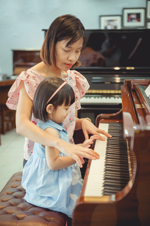 The cute little girl is learning piano with the teacher.の写真素材