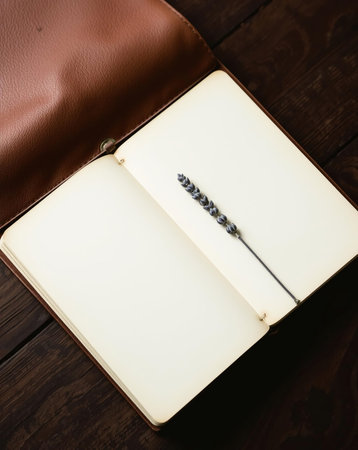 An open notebook with blank pages and a sprig of lavender on a dark wooden table.の素材
