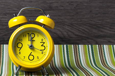 Yellow retro alarm clock on color mat shows 12 oclock