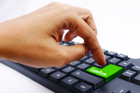 Finger pressing computer keyboard with highlight COMFIRM key over white backgroundの写真素材