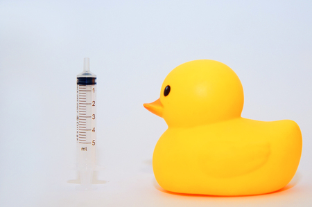 yellow duck toys and syringe over white backgroundの写真素材
