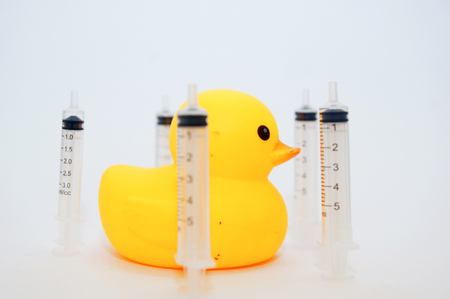 yellow duck toys with syringe over white backgroundの写真素材
