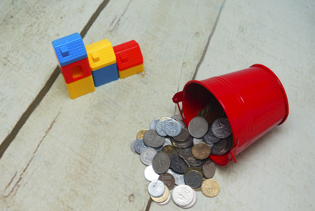 red aluminum bucket spill out coins and house toy over wooden floorの写真素材