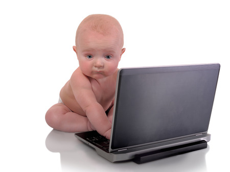 Image of a baby boy sitting in front of a laptop computer staring at the cameraの写真素材