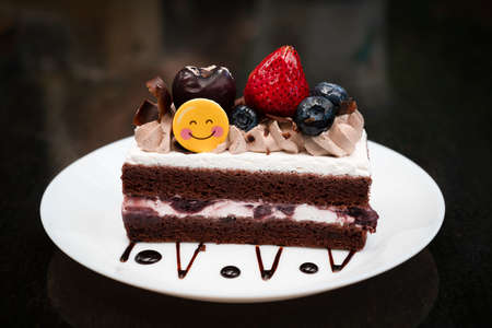 Piece of chocolate cake homemade with strawberry, blueberry and white cream toppings on a white...