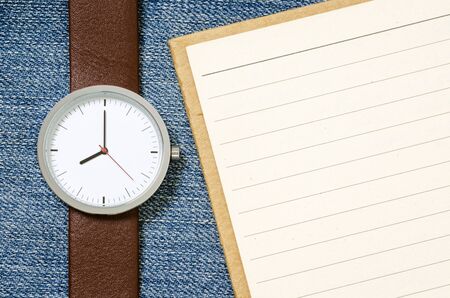 watch and notebook with blank pages on blue jeans