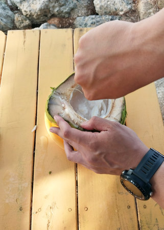 A close-up of hands skillfully cutting open a fresh coconut on a sunny beachside table, revealing...