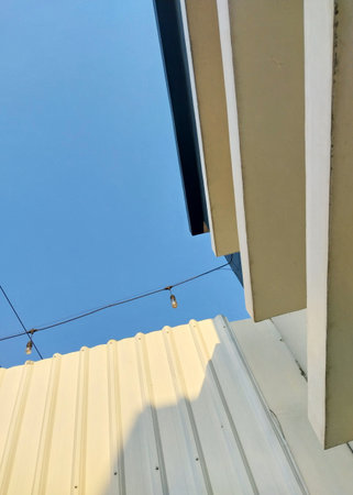 Minimalist outdoor scene featuring a clear blue sky, string lights, a modern beige wall, and part of...