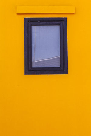 square glass window and black wood frame on bright yellow painted cement wall textureの写真素材