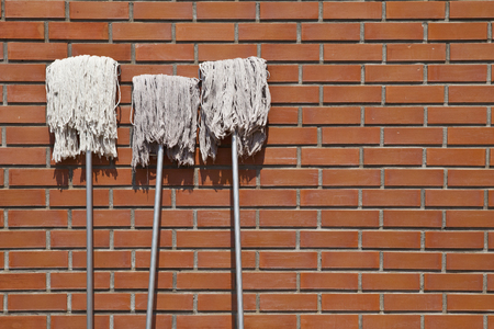 three white mops lean against brick wall revealed to sunlight explosureの写真素材