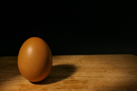 yellow colored egg on black background. Selective focus. Light and shadow.の写真素材